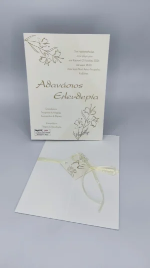 Κρεμ προσκλητήριο γάμου με χρυσές γραμμές λουλουδιών, καρτάκι με μονογράμματα και κορδελάκι.